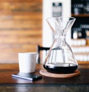 A photo of a glass carafe with coffee on a table with a cup and mobile phone.