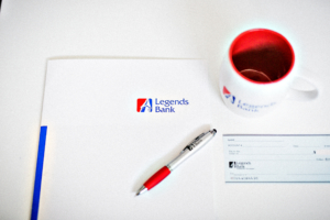 A photo of a desk with a Legends Bank folder, pen, check, and cup.