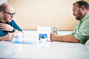 A photo of two people sitting across from each other, with Legends Bank drinkware.