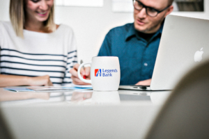 A photo of a Legends Bank coffee cup. In the background is two people discussing paperwork.