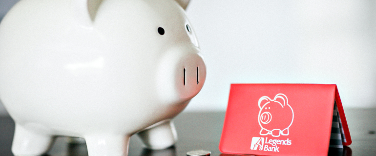 A photo of a piggy bank with coins next to a Legends Bank savings booklet.